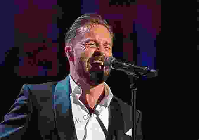 Alfie Boe Performing Onstage With A Microphone In Hand, Captivating The Audience With His Powerful Voice. Blood Brother Alfie Boe